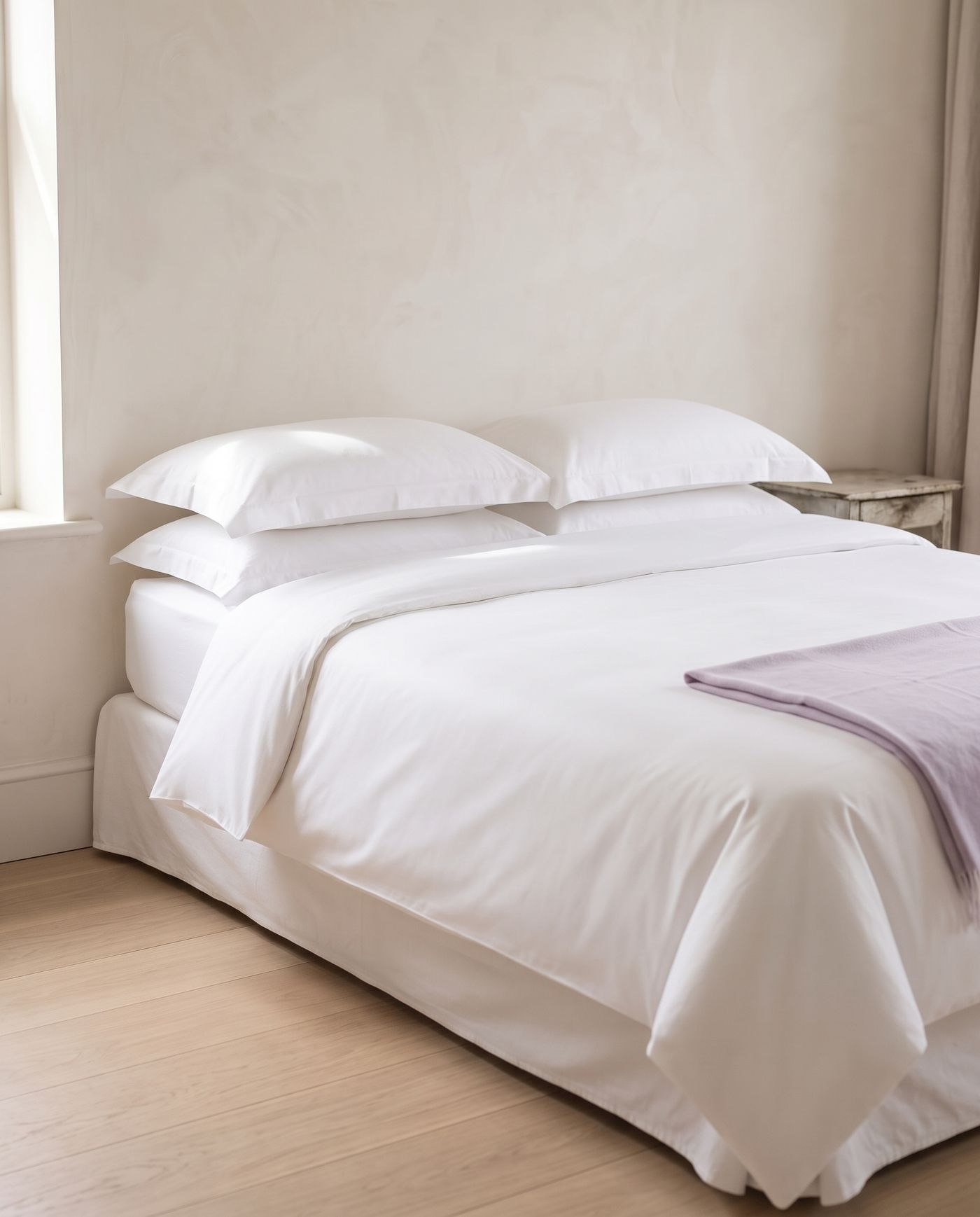 A made bed in crisp, pressed white cotton with a lavender throw at the foot